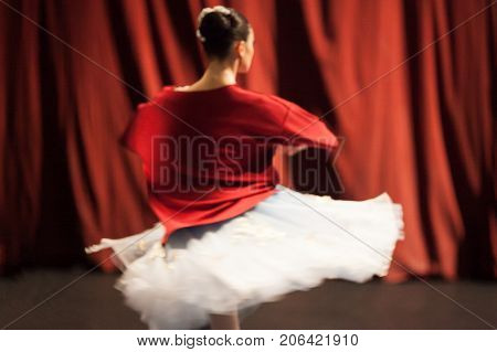 ballet, mystic, rehearsal concept. tender and phantom figure of ballerina, photographed out of focus, spinning around herself and her bright red shirt blending in with the curtains of theater