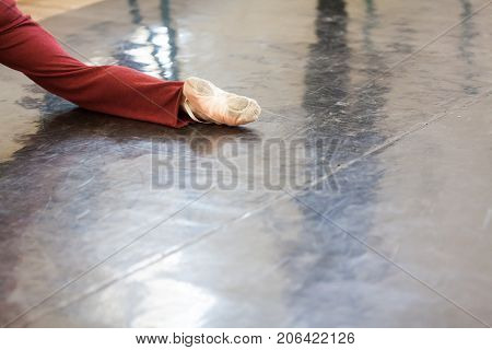 dancing, pation, strength concept. close up of muscular leg of man who dancing in the class for rehearsal wearing in burgundy-red sweatpants and light-pink satin pointe shoes