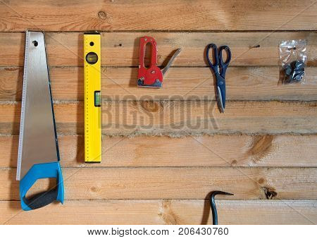 Tools for building on wooden background of pine forest. Bright yellow level saw scissors hanging on the wall on the screws. Between the pine rail laid with linen tape.