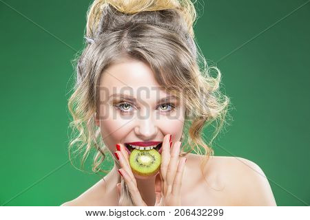 Fruit Series. Portrait of Curious Caucasian Blond Model Posing With Slice of Green Juicy Kiwi Fruit and Her Mouth. Against Green Background. Horizontal Image Composition