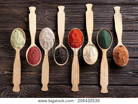 Different colorful superfood powders in spoons on wooden table