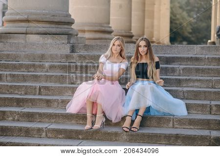 Two beautiful girls in colored skirts sit on stairs