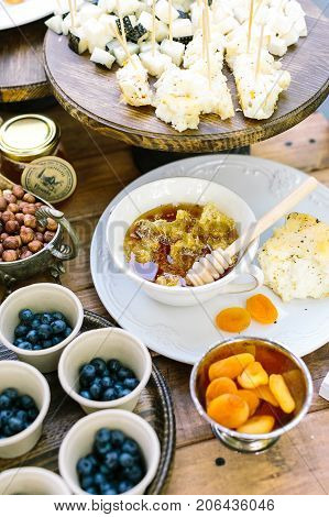 housemade, meal, dessert concept. table setting with numbers of such treats as nuts, berries, dried apricots, nearby with little dish of honey and homemade bread