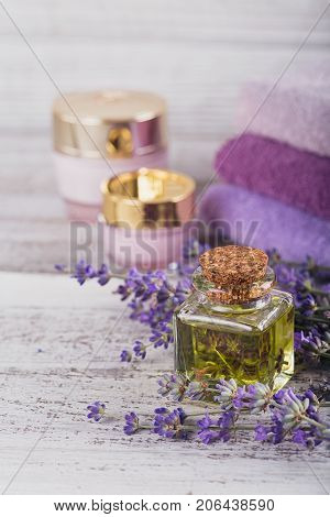 Bottle of essential oil and fresh lavender flowers on a white wooden background. Aromatherapy spa and wellness concept