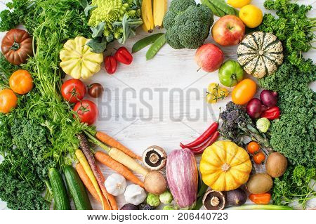 Colorful frame made of fresh raw vegetables, fruits herbs on white wooden background, copy space for text in the middle, top view, selective focus