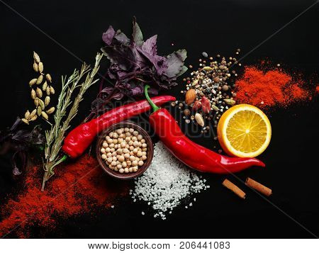Two red pods of chili pepper, a slice of fresh orange, various fragrant species on a black background. Close-up of vegetables. Copy space.