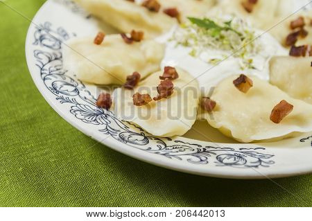 Cooked dumplings with cheese pork scratching and creme fraiche on wooden table. Polish ukrainian russian traditional food.
