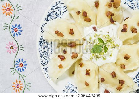 Cooked dumplings with cheese pork scratching and creme fraiche on wooden table. Polish ukrainian russian traditional food.