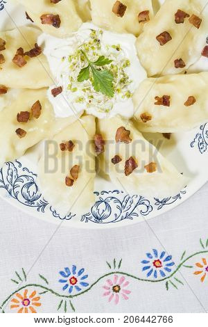 Cooked dumplings with cheese pork scratching and creme fraiche on wooden table. Polish ukrainian russian traditional food.