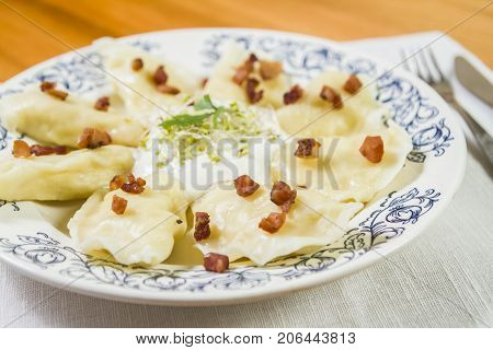 Cooked dumplings with cheese pork scratching and creme fraiche on wooden table. Polish ukrainian russian traditional food.