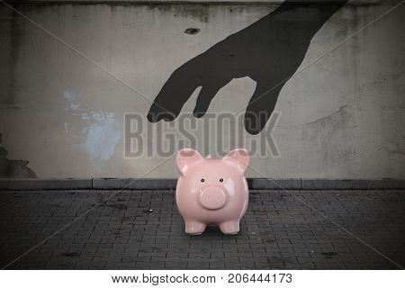 Close-up Of Silhouette Hand Picking Up Piggy Bank On Street