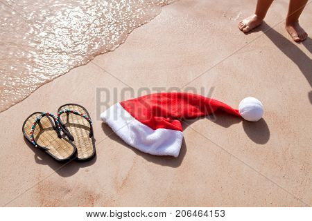 Santa's hat and women's slap on the shore of the Red Sea. Baby naked legs on the sand. Celebrating the new year at the resort