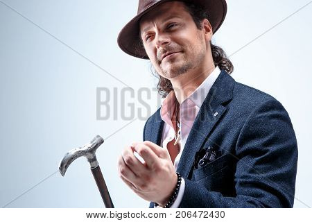 The mature bearded man in a suit and hat holding cane. Isolated on a gray studio background.
