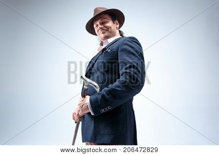 The mature bearded man in a suit and hat holding cane. Isolated on a gray studio background.
