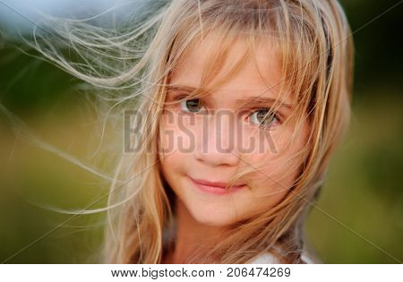 Portrait of the charming girl of 9-10 years. Wind plays with long blonde hair. Serious look of big green eyes. Gentle half-smile.