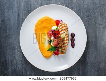 Grilled turkey fillet with pumpkin puree and vegetables on white plate. Close view