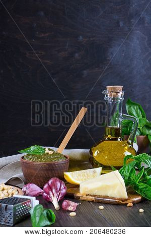 Tradizione Italiana Homemade Pesto recipe ingredients on dark table. Parmesan cheese, basil leaves, pine nuts, olive oil, garlic.