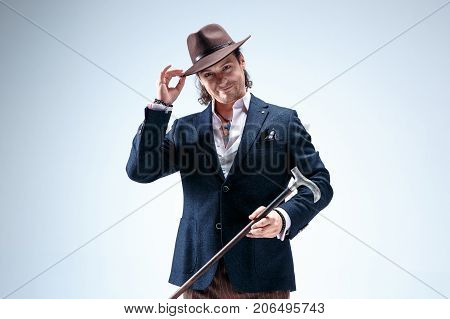 The mature man in a suit and hat holding cane. Isolated on a gray studio background.