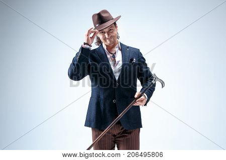 The mature man in a suit and hat holding cane. Isolated on a gray studio background.