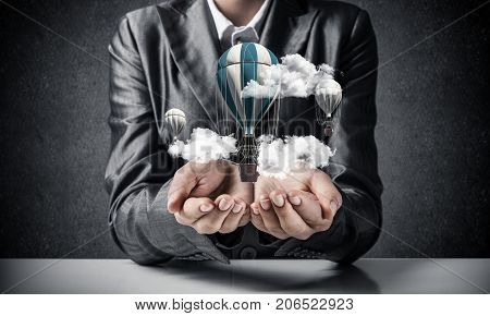 Closeup of business woman in suit presenting flying aerostate among clouds in her palms with dark wall on background. 3D rendering.