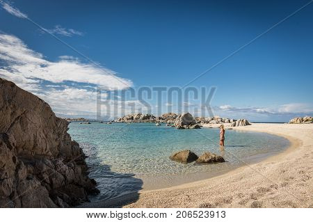 Woman in bikini paddling in the translucent Mediterranean sea just off a deserted sandy beach on Cavallo island near Corsica in France with translucent Mediterranean and blue sky