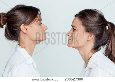 Studio profile portrait of young female twins sisters on gray