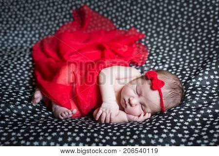 Sleeping pretty newborn in red dress and a small ribbon on his head.