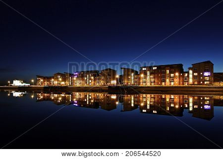 Quayside Apartment Building at night with reflections in the water.