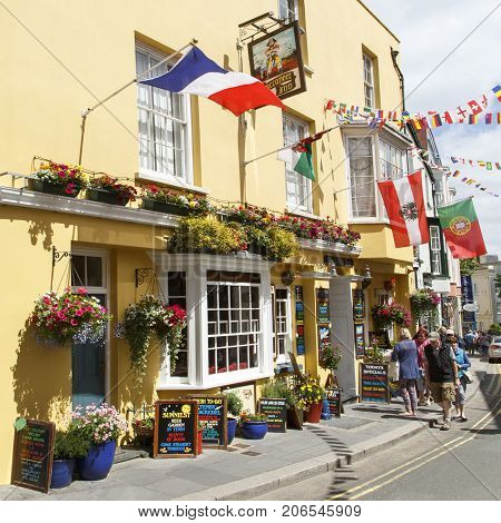 Tenby, UK: July 05, 2016: Tourists walk past the brightly painted Buccaneer Inn in Tenby. A very popular pub with visitors during the summer time with its flags and hanging baskets.