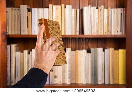 Male hand holding a book in front of bookshelves