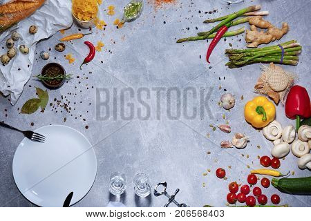 Top view of red chili pepper, cloves of garlic, mushrooms, salad pepper, corkscrew, white plate, seasonings, ginger, tomatoes, cucumbers on a light gray background.