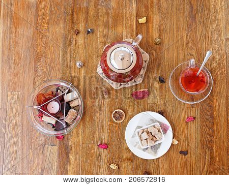 Top view of a composition of traditional breakfast. A plate of powdered cookies, chocolate sweets and biscuits on a wooden table background. A cup of red tea and strawberry spicy tea in a kettle.
