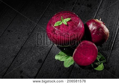 Beautiful dark beetroot cocktail with mint in a transparent glass on a dark wooden background. Natural vegetables and green salads. Healthy restaurant beverages and juices. Copy space.