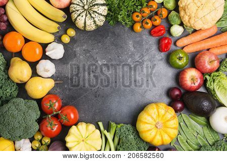 Assortment of vegetables and fruits arranged in a circle on the dark grey background, copy space for text in the middle, top view, selective focus