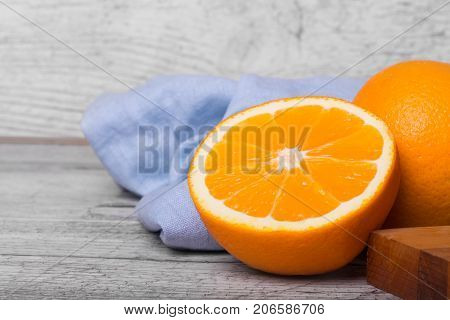 A gray wooden table with unpeeled vivid health-giving oranges full of vitamins, a wooden board and a blue napkin on a light gray wooden background.