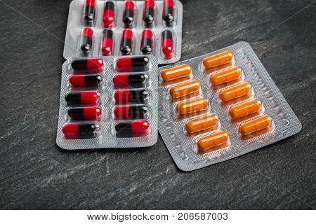Close-up of different packs of meds on a light gray table background. Multi-colored capsules in blisters. An assortment of drugs, antibiotics, painkillers, pills to cure a sickness.