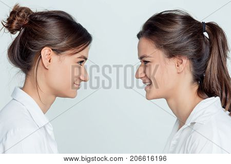 Studio profile portrait of young female twins sisters on gray