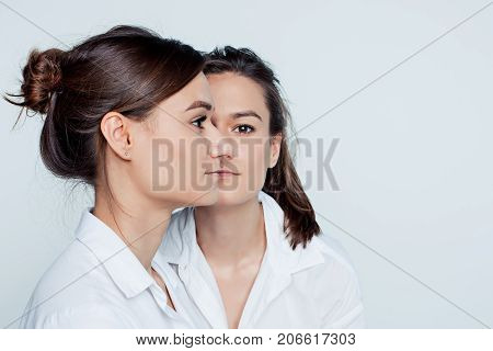 Studio profile portrait of young female twins sisters on gray