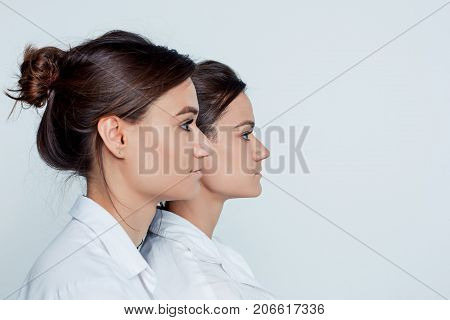 Studio profile portrait of young female twins sisters on gray