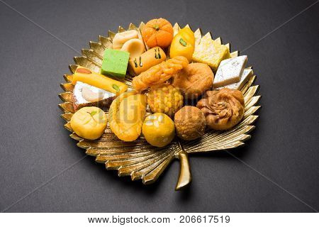 stock photo of Indian sweet or mithai and oil lamp or diya with gift box and flowers on decorative or colourful background, selective focus