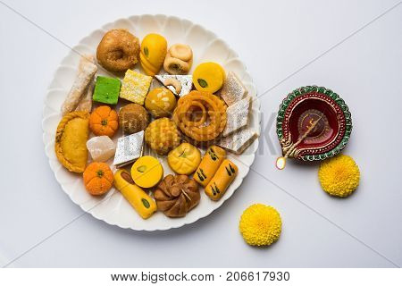 stock photo of Indian sweet or mithai and oil lamp or diya with gift box and flowers on decorative or colourful background, selective focus