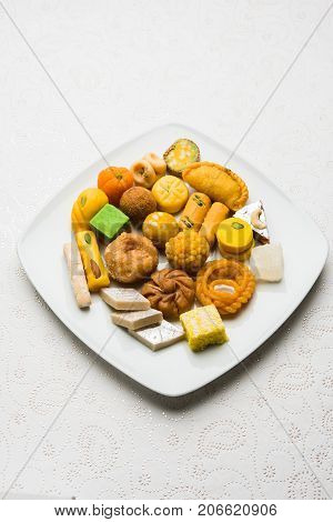 stock photo of Indian sweet or mithai and oil lamp or diya with gift box and flowers on decorative or colourful background, selective focus