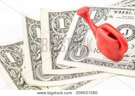 One Red Watering Can Laying On Four One Dollar Banknotes