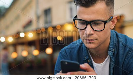 Close Up Shot Of Attractive Man In The Stylish Glasses Using Cell Phone For Chatting With Friends In