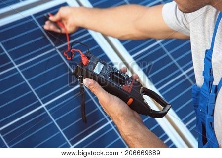 Young worker checking installation of solar panels by using multimeter