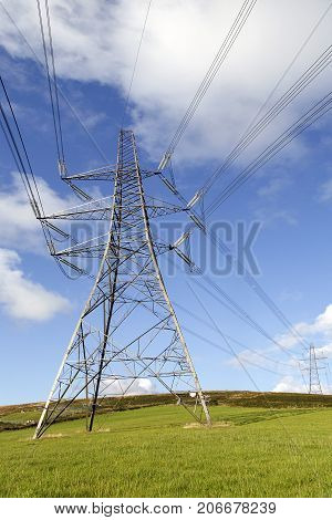 Electricity pylons traversing the Welsh countryside with a blue sky background in a vertical format