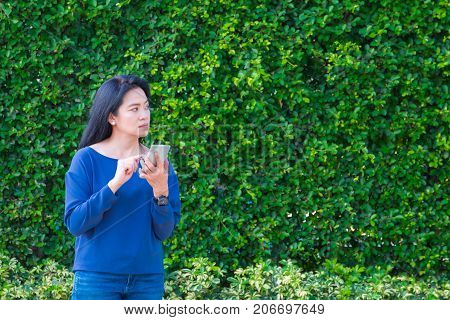 Asian woman in causal cloth and smile while use mobile phone outside house at green hedgeLeave copy space for adding your text