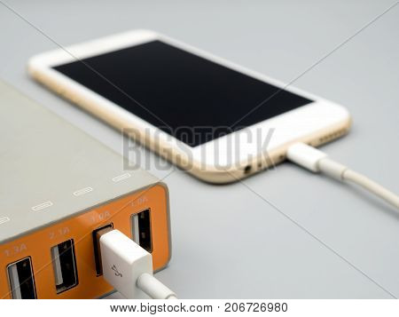 Close-up image of smart phone charging with multiport USB power adaptor on gray background Selective focus