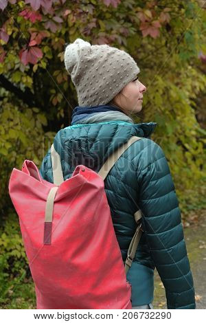 Young female with rucksack walking in the autumn park vertical outdoor shot