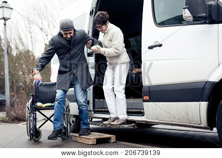 nurse helping senior man exit a van and get to his wheelchair